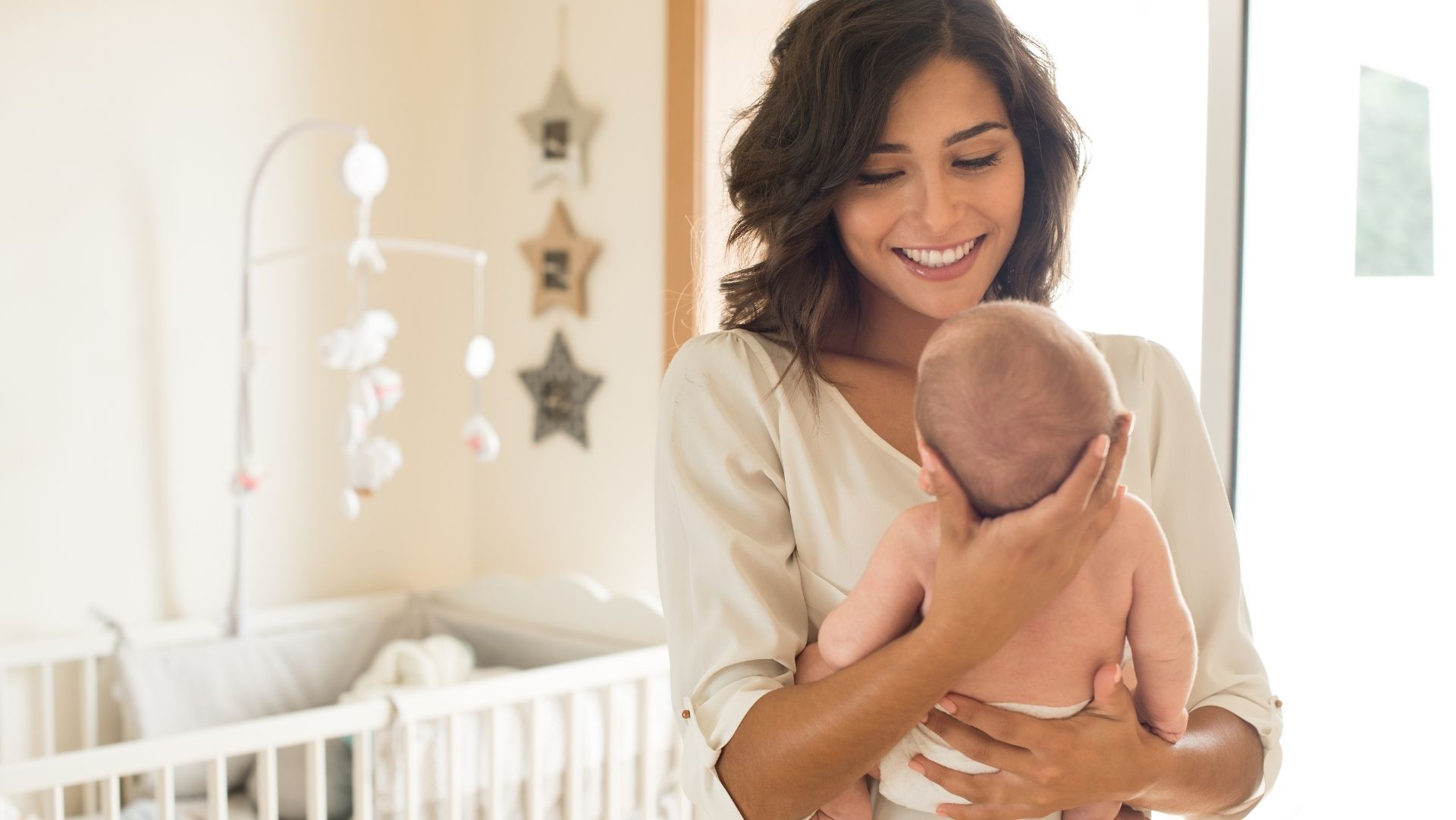 Mother holding her newborn baby in the nursery. Smiling and at peace postpartum.